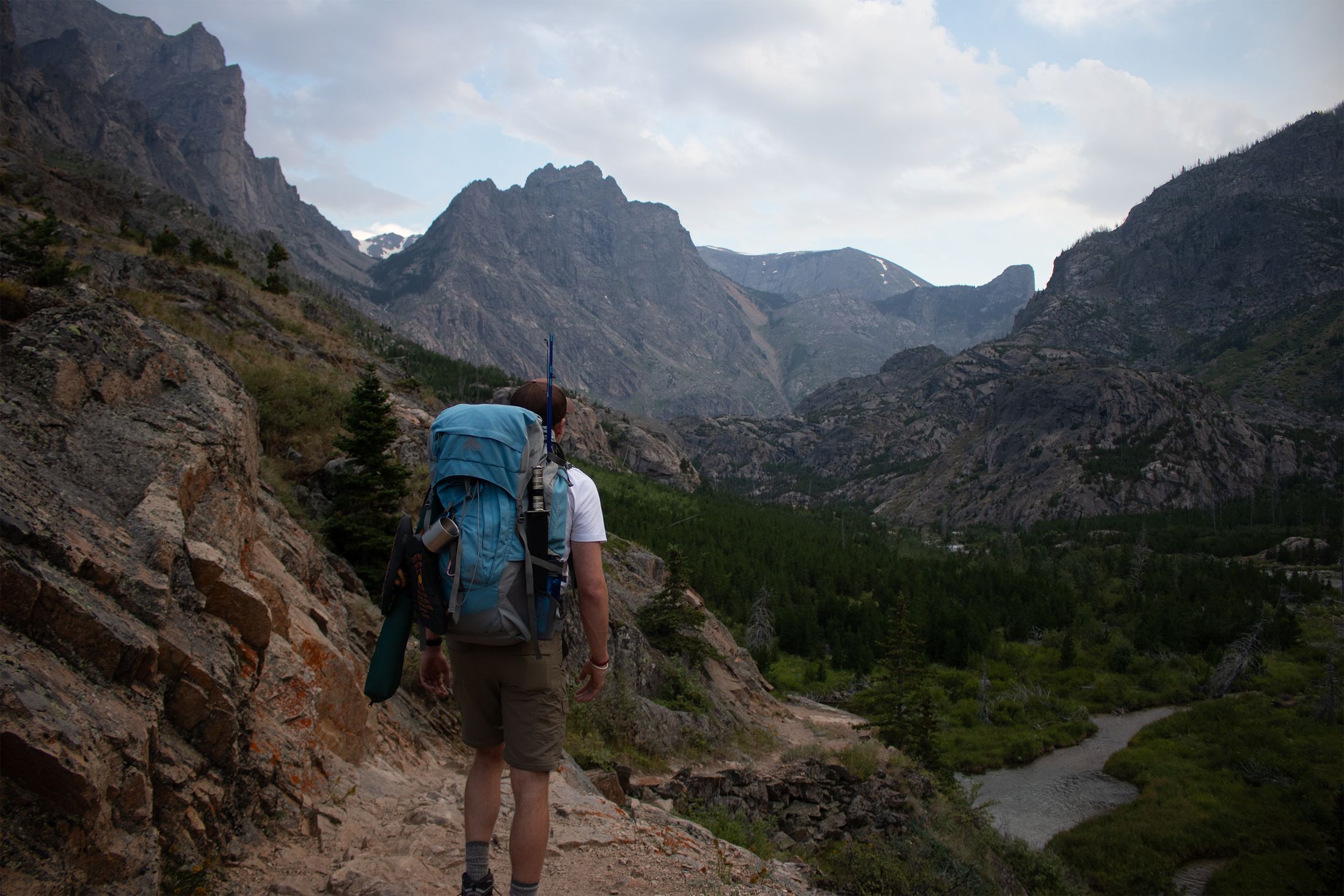 A backpacker on a rocky trail looking up a deep glacial valley toward jagged peaks